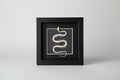 Decorative wall art with a snake design in a black frame on a light gray background